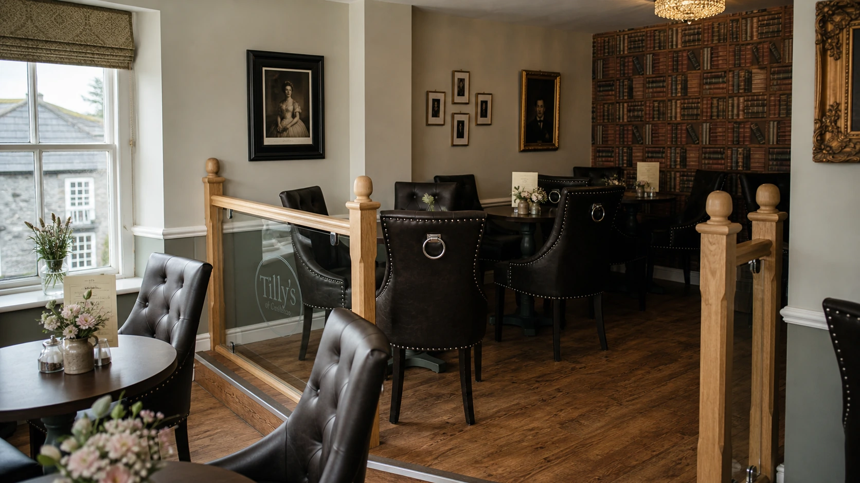 The raised parlour at Tilly's — leather tub chairs, library-book wall, oak railing with etched Tilly's glass